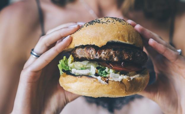 Una mujer, comiendo una hamburguesa./
