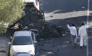 Dos especialistas se acercan al coche patrulla en el que viajaban los dos guardias civiles muertos por la explosión de la bomba. /AFP/