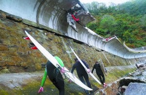 Tres surfistas sortean las piedras arrastradas por el oleaje al pie del paseo peatonal entre Zarautz y Getaria, de donde se desprendieron quince metros de muro. :: ETXEBERRIA/