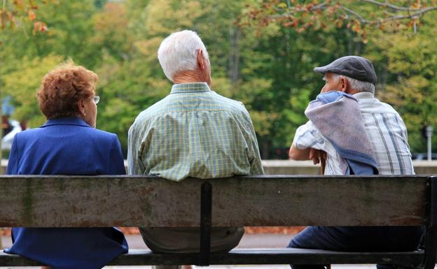 Tres personas mayores descansan en un banco de la calle, mientras comparten conversación./