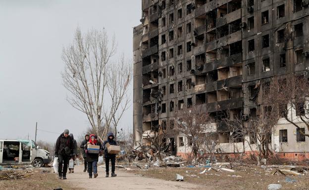 A group of people carrying boxes in front of a flattened building in Mariupol.