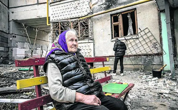 A woman sitting on a bench in front of a completely destroyed building in Kharkov.