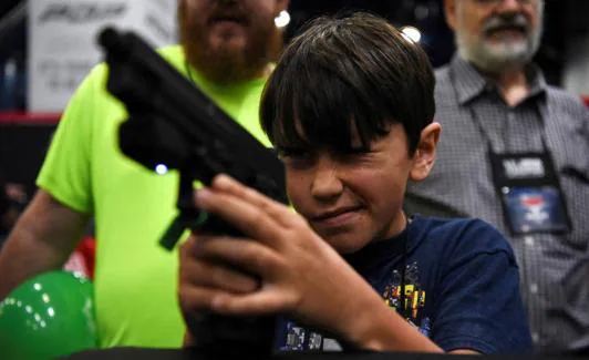 A boy tries out an electronic weapon in a virtual targeting game during the National Rifle Association convention