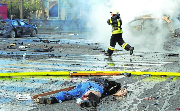 A firefighter runs past the body of a victim lying on the asphalt after a missile explosion on a kyiv street. 